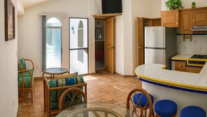 A compact kitchen with a refrigerator, wooden cabinets, and a dining area with a glass table and wicker chairs.