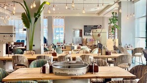Un restaurant avec des chaises à rayures, des ampoules suspendues et de grandes fenêtres.