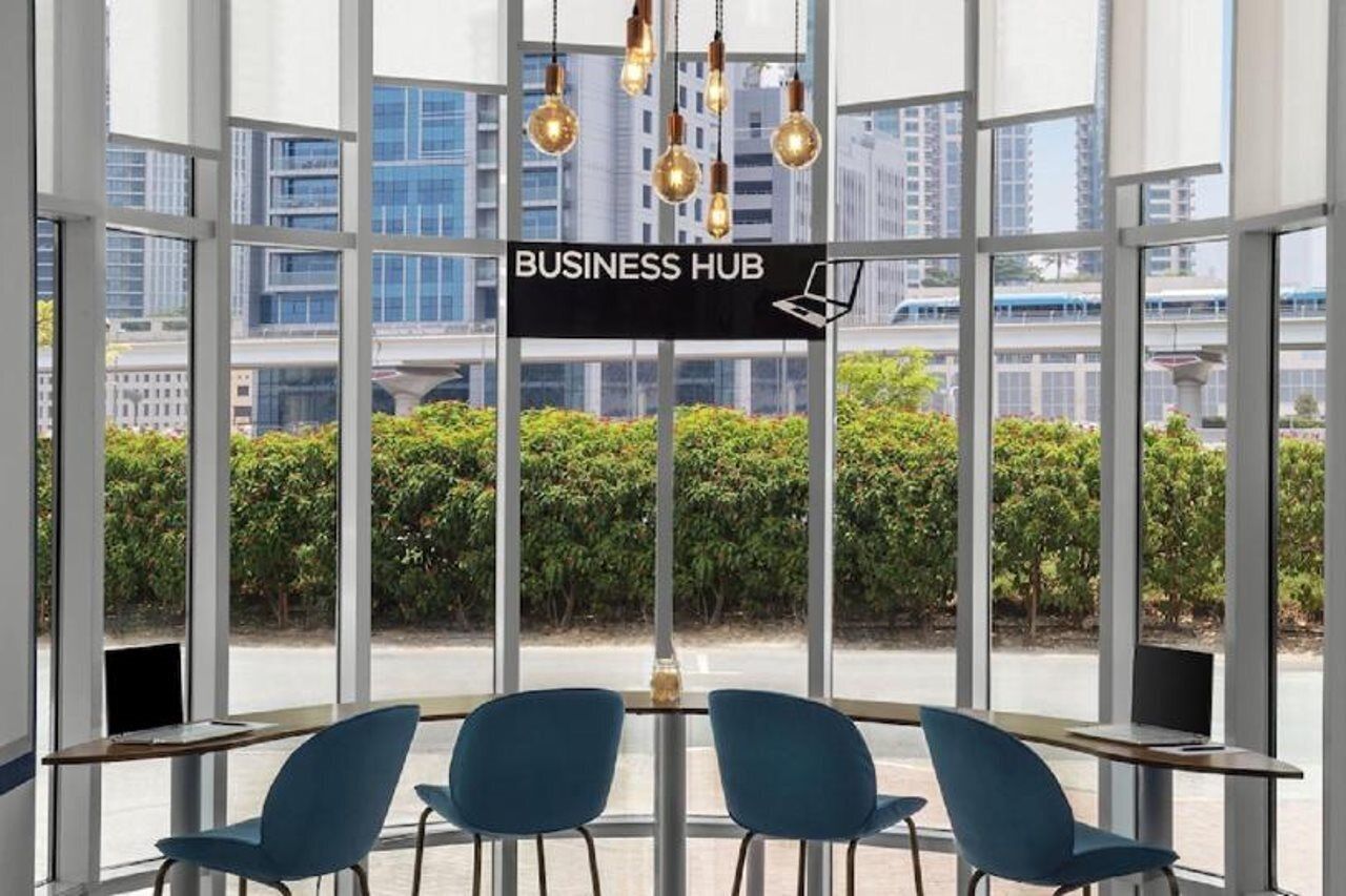 A modern indoor space with large windows, a sign reading 'BUSINESS HUB,' and a view of a cityscape.