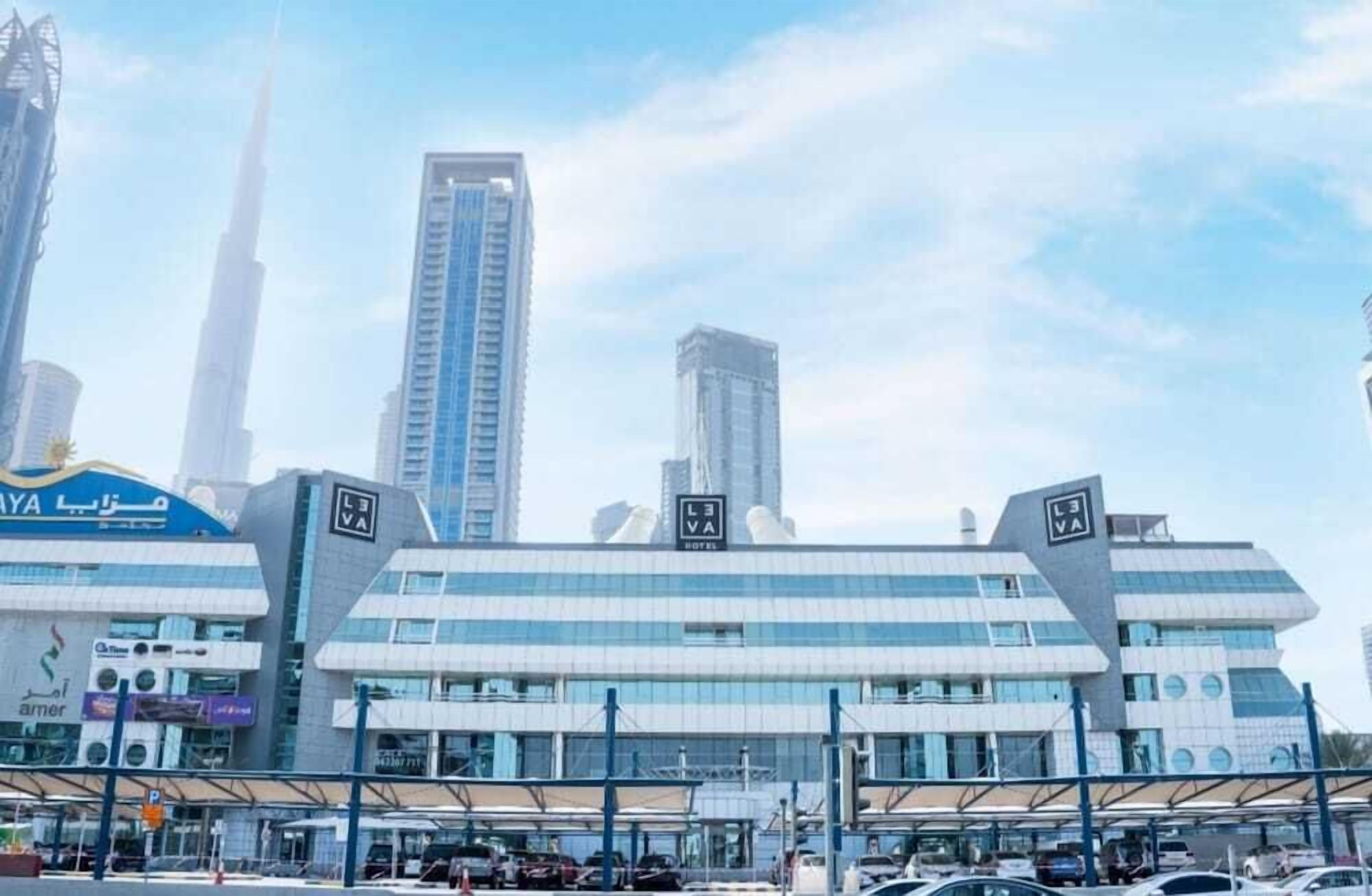 A modern hotel with a prominent LEVA sign, a large parking lot, and surrounding high-rise buildings.