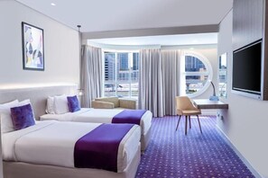Ein Hotelzimmer mit zwei Betten, einem Schreibtisch, einem Stuhl, einem Fernseher und einem großen Fenster mit Vorhängen.