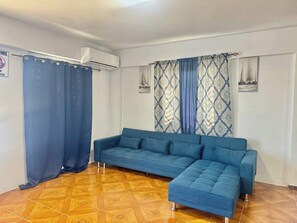 Ein Zimmer mit einem blauen Sofa, gemusterten Vorhängen und einem Fliesenboden.