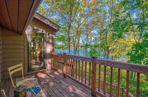 Une terrasse en bois avec une rambarde, une porte vitrée donnant sur une pièce et une vue sur les arbres.