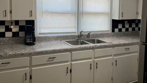 A kitchen with white cabinets, a double sink, and a coffee maker.