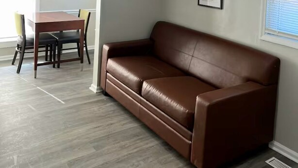 A living room with a brown leather sofa, a dining table with chairs, and a ceiling light fixture.