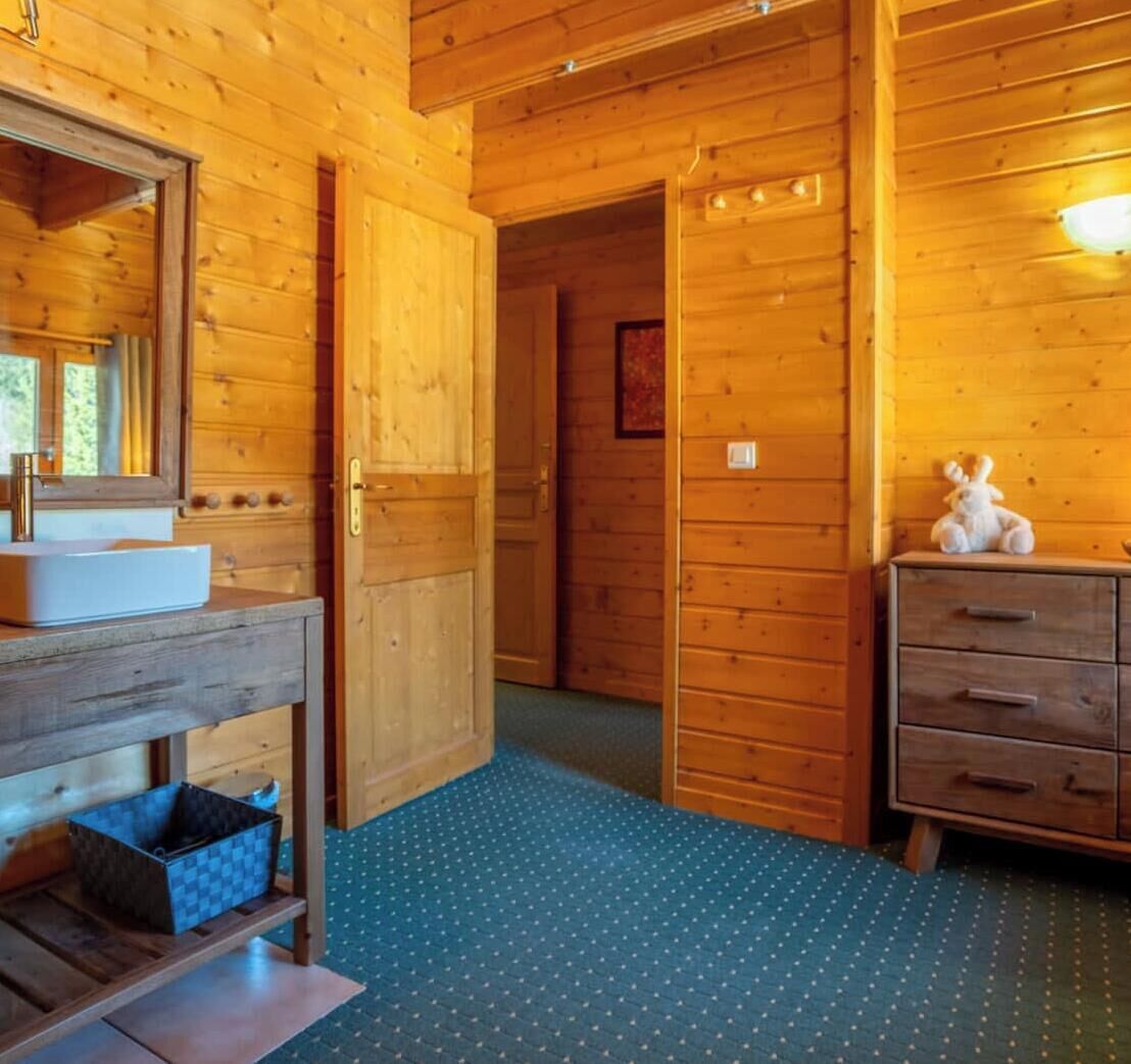 A wooden cabin interior with a bathroom, a dresser, and a mirror.