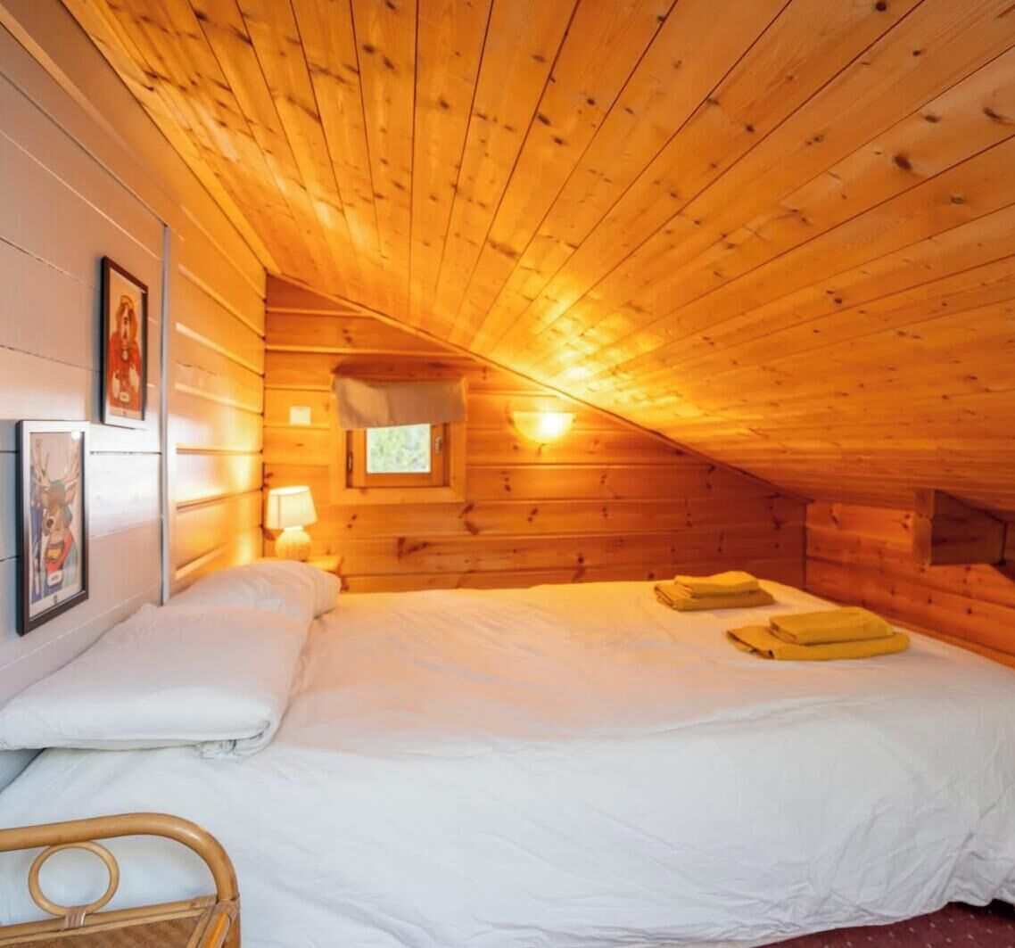 A wooden cabin room with a bed, a nightstand, a lamp, and framed pictures on the wall.