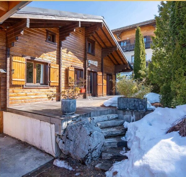 Una cabaña de madera con un porche cubierto, escalones de piedra y nieve en el suelo.