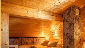 Ein gemütliches Schlafzimmer in einer Holzhütte mit einem Bett, Kissen, einem Fellteppich und einem hölzernen Kopfteil.
