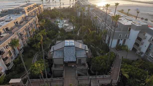 Un resort con varias edificaciones, una estructura central con techo de cristal y un área de piscina rodeada de palmeras.