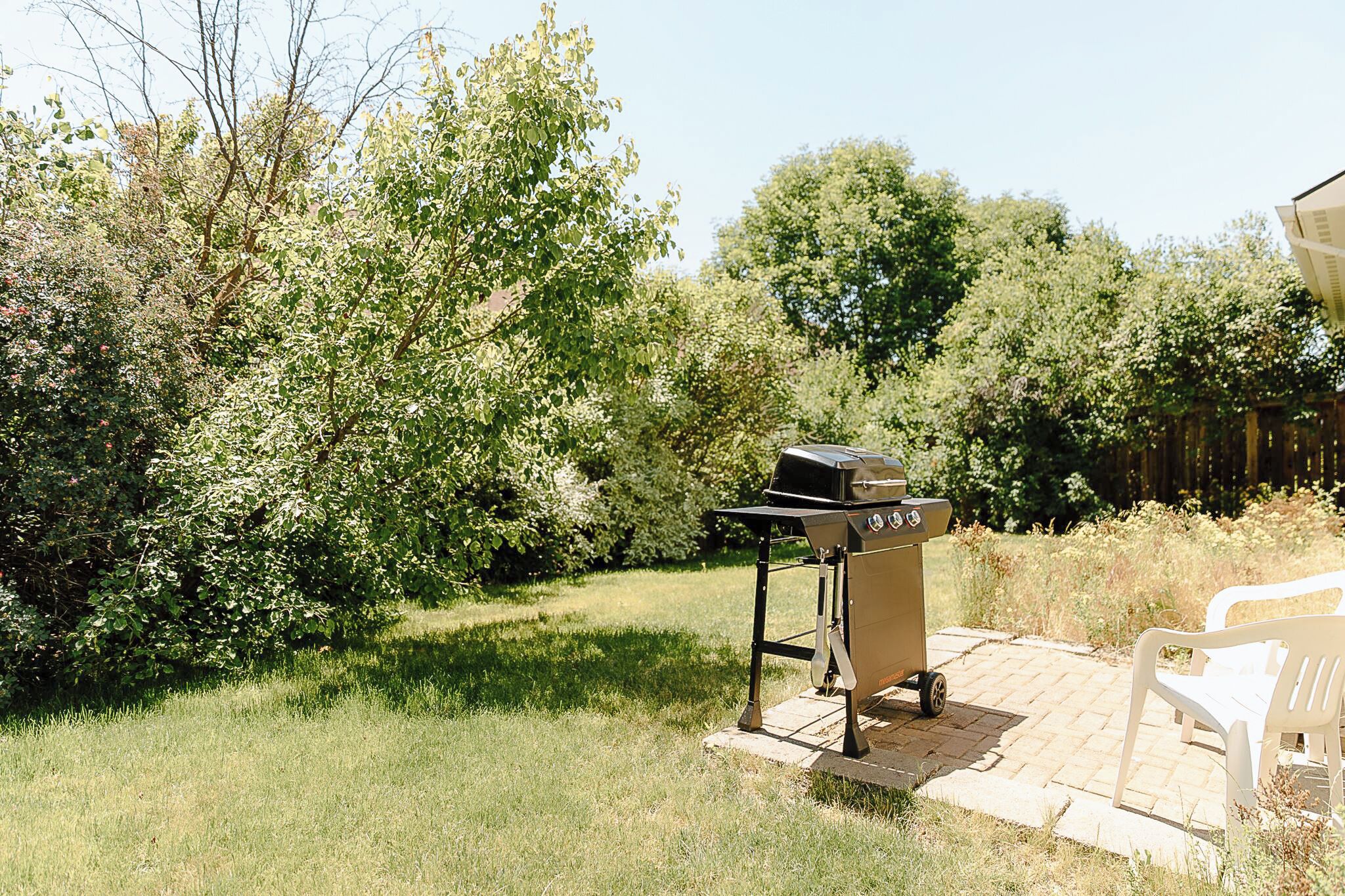 Une terrasse avec un barbecue, un banc blanc et une végétation luxuriante.