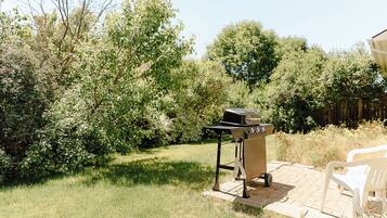 Une terrasse avec un barbecue, un banc blanc et une végétation luxuriante.