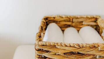 A wicker basket with cylindrical objects, possibly candles, on a white surface against a plain wall.