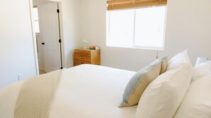 A bedroom with a bed, a nightstand, a window with blinds, and a door. - The Lighthouse - Entire home in Moscow, Idaho (Moscow)