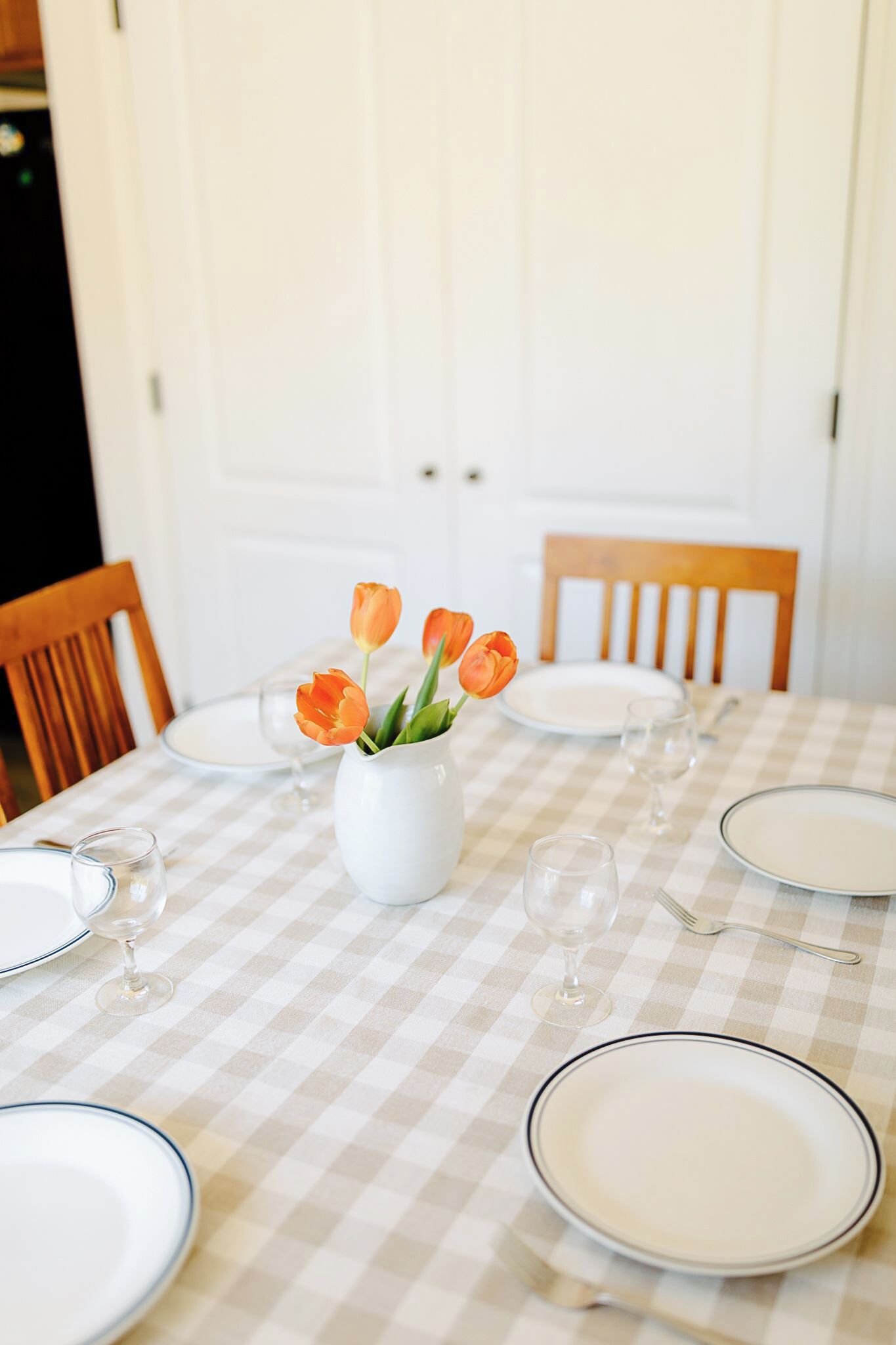 Taula de menjador preparada amb plats, gots i un botic de tulipes.