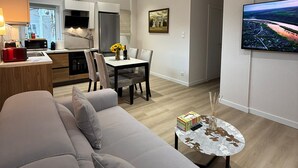Un salon moderne comprenant un canapé, une table à manger avec des chaises, un coin cuisine avec des placards et un réfrigérateur, et un téléviseur fixé au mur.