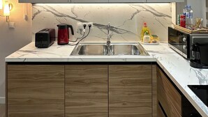 Une cuisine moderne dotée d’un plan de travail en marbre, de meubles en bois, d’un évier encastré, d’un grille-pain, d’une machine à café et d’un four à micro-ondes.