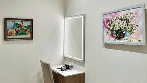Une pièce comprenant un bureau, un climatiseur, un tableau encadré représentant des fruits et un tableau encadré représentant des fleurs.