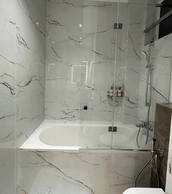 Ein modernes Badezimmer mit einer Glasdusche, einer freistehenden Badewanne und Marmorwänden.