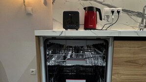 Un lave-vaisselle Bosch ouvert, avec son panneau de commande, une bouilloire rouge de la marque Bosch et un pare-feu en marbre dans la cuisine.