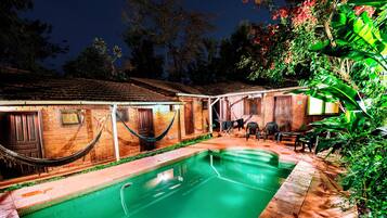 Piscina com casa de tijolos, redes e mobiliário de exterior.
