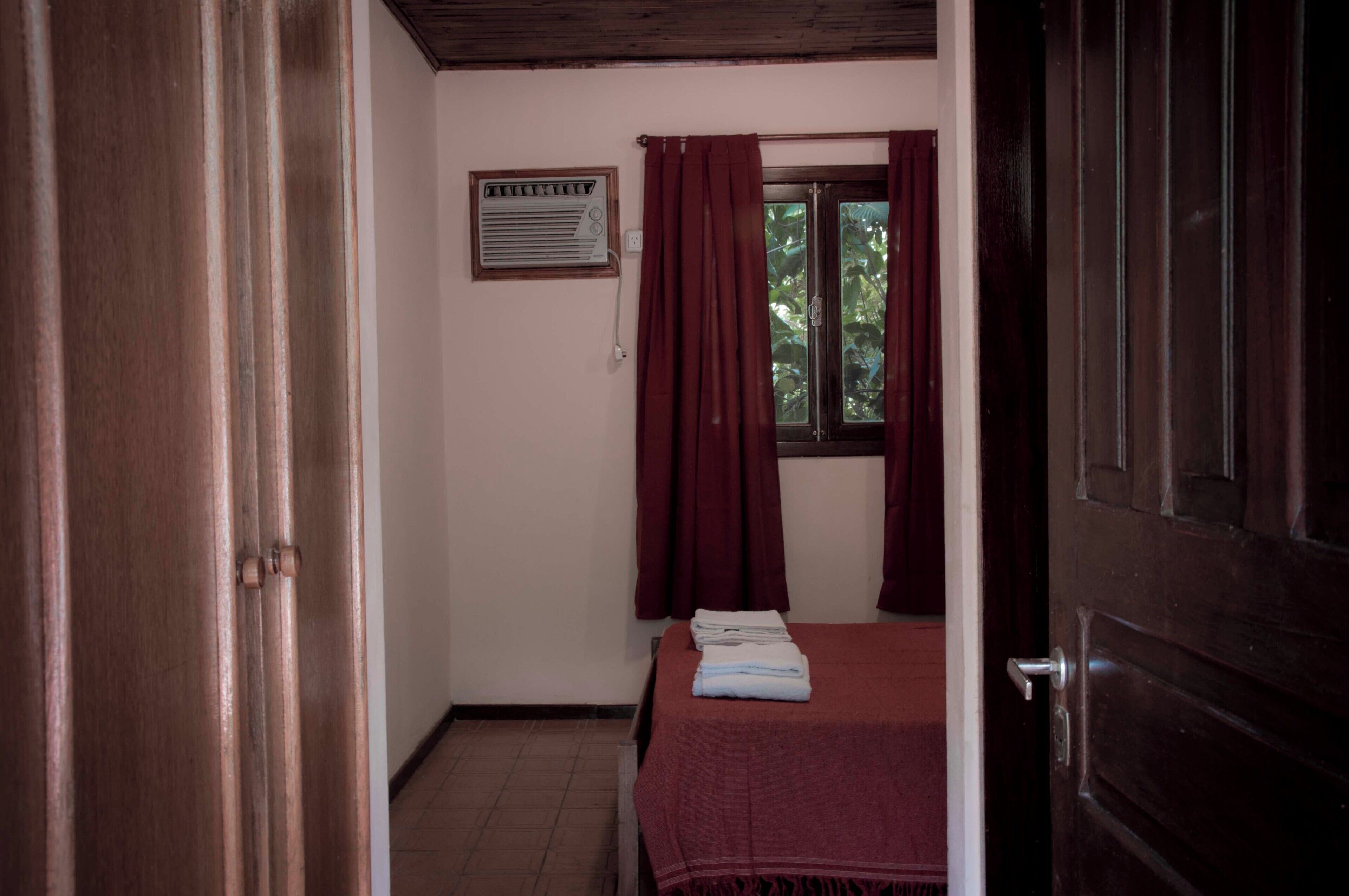 Ein Zimmer mit Bett, einem Fenster mit Vorhängen, einem Heizkörper und einer Tür.