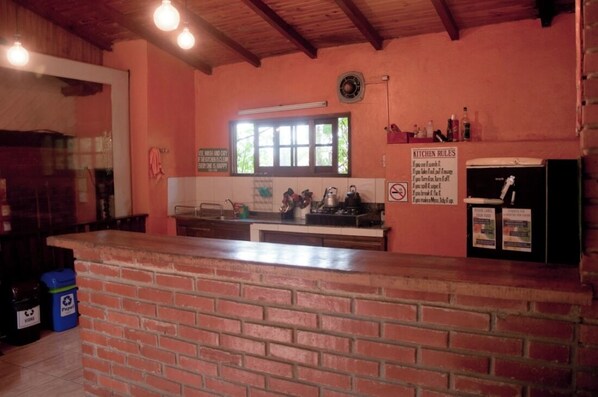 A kitchen with a brick counter, a window, and a sign listing kitchen rules. - Poramba Hostel (Puerto Iguazú)