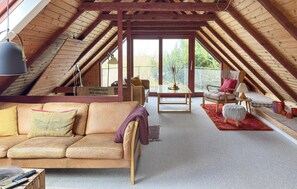 A cozy attic room with a wooden ceiling, a sofa, a chair, a table, and a view through large windows. - Cozy home in Glesborg with WiFi (Glesborg)