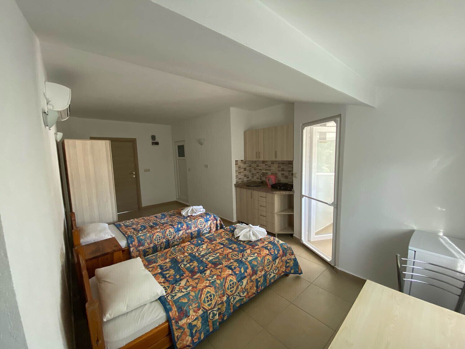 A room with two beds, a kitchenette, and a door leading to another room.