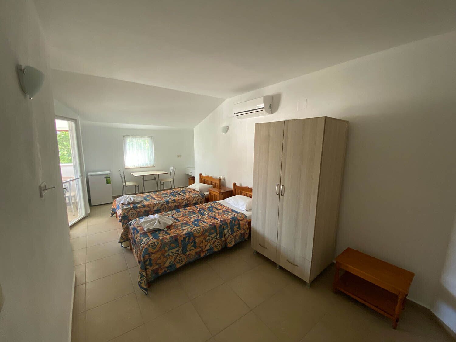 A bedroom with two beds, a wardrobe, a small table, and a window.