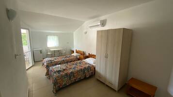 Une chambre avec deux lits, une armoire, une petite table et une fenêtre.