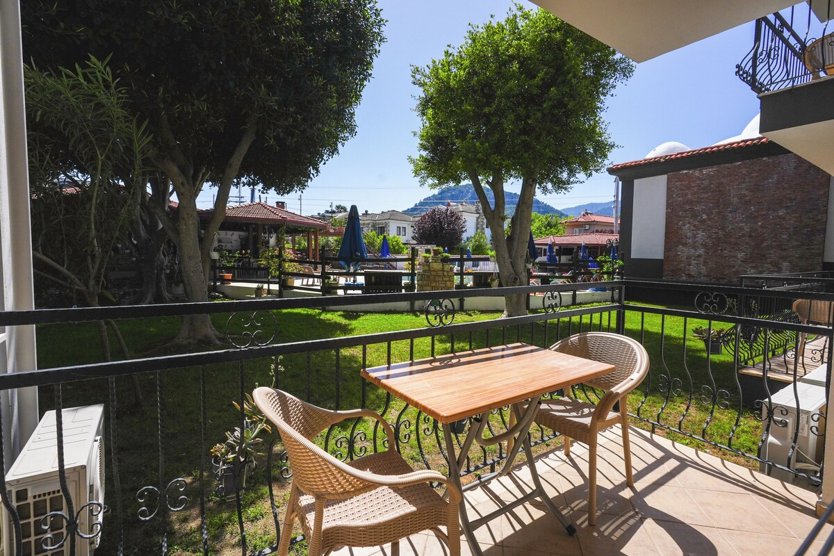 A balcony with wicker furniture, a view of a park, and a building in the background.