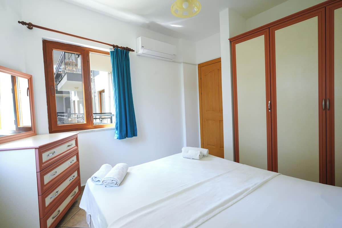 Ein Schlafzimmer mit Bett, Kommode, einem Fenster mit Vorhängen, einer Klimaanlage und einem Kleiderschrank.