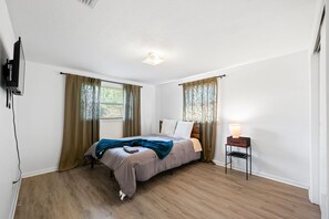 A bedroom with a bed, curtains, a lamp, and a television. - 3-bedroom apartment with AC in Jacksonville (Jacksonville)