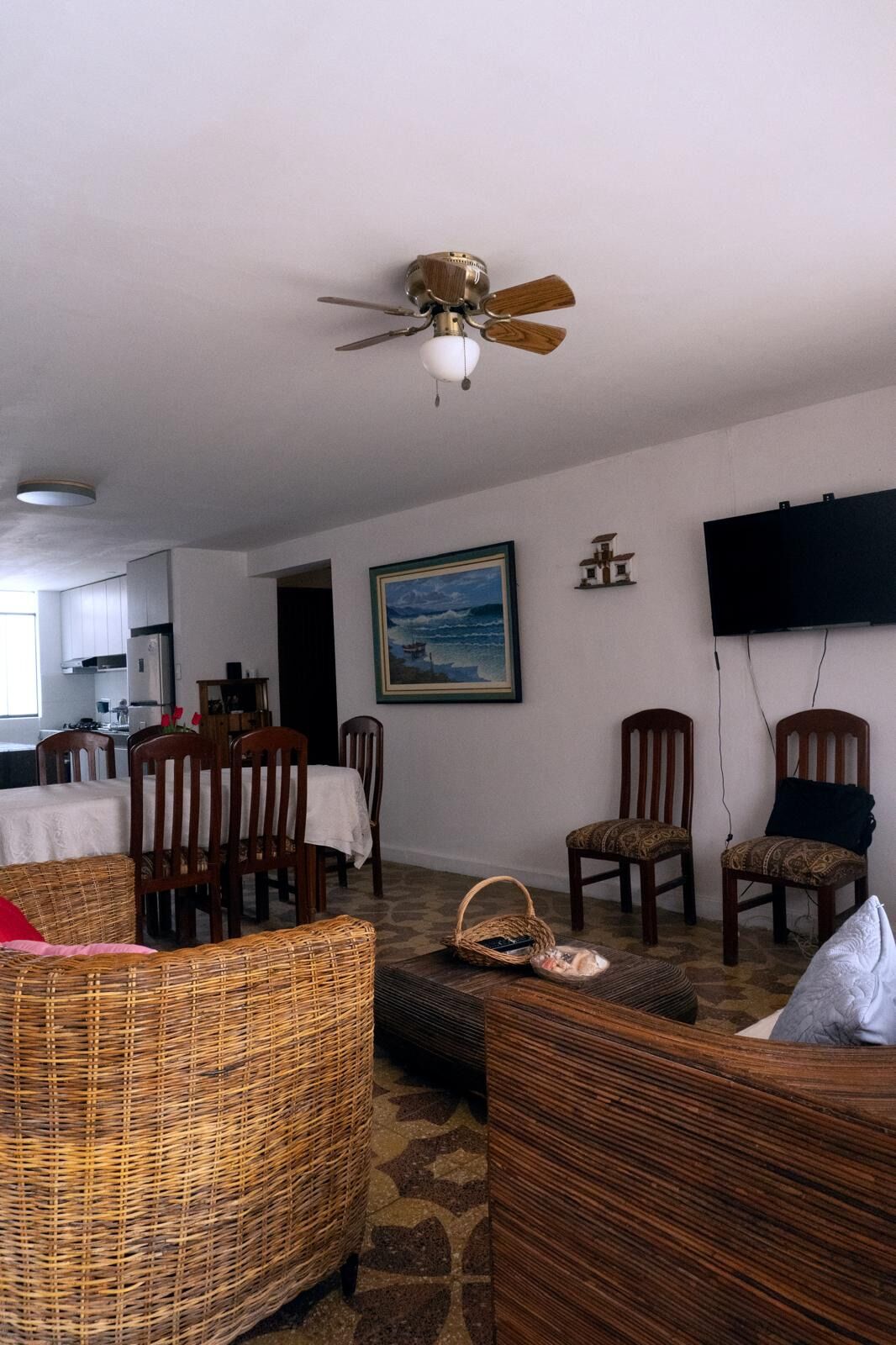 A living room with a ceiling fan, a television mounted on the wall, a dining area with chairs and a table, and a painting on the wall.
