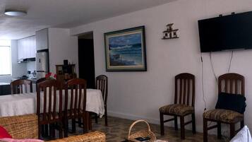A living room with a ceiling fan, a television mounted on the wall, a dining area with chairs and a table, and a painting on the wall.