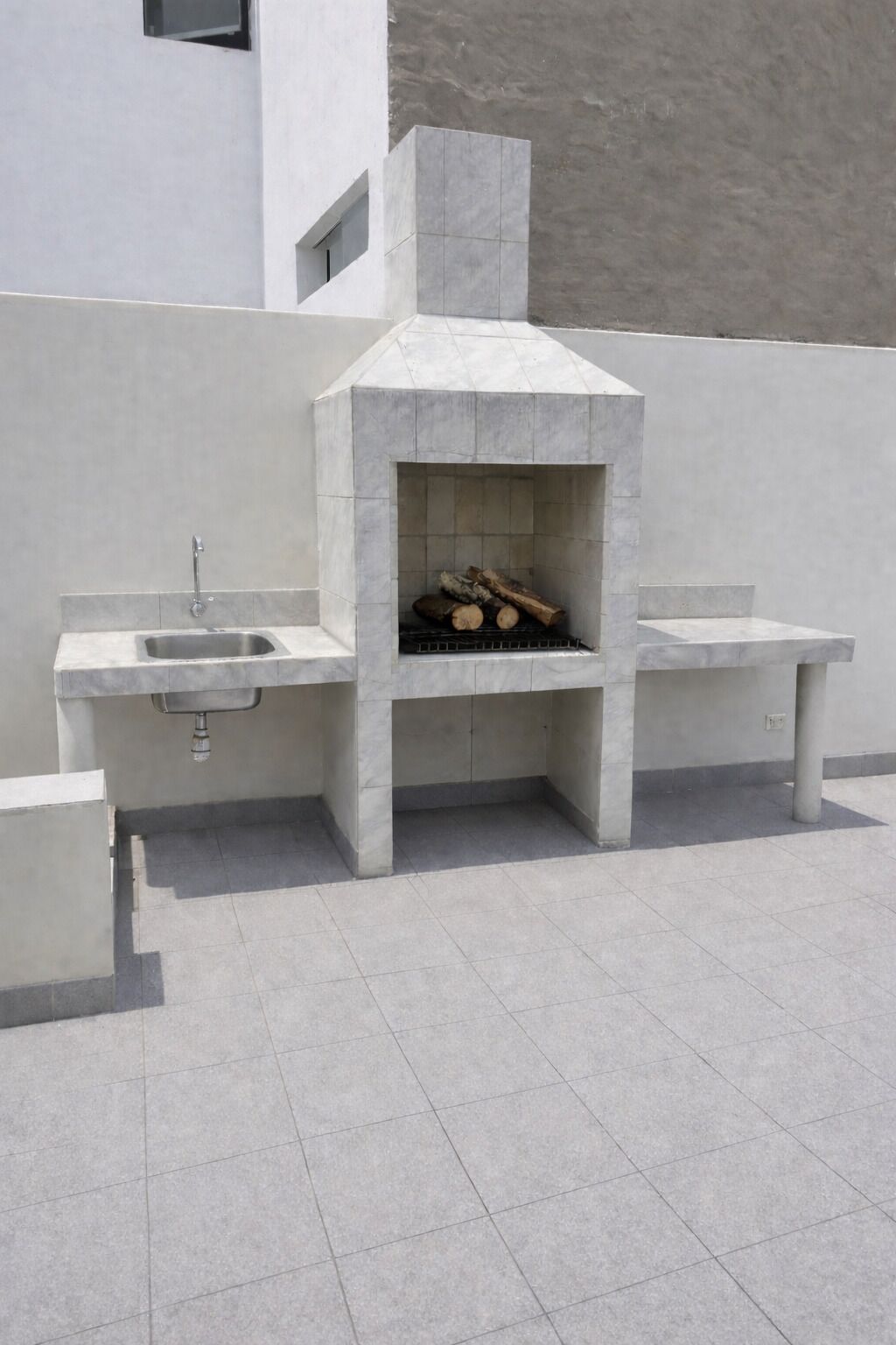 A modern outdoor kitchen with a built-in grill, a sink, and a bench.