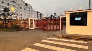 Ein begrenzter Zugang zu einem Gebäude, mit einer Fußgängerüberweg, einer kleinen Verkaufshütte und einem mehrstöckigen Wohnhaus im Hintergrund.