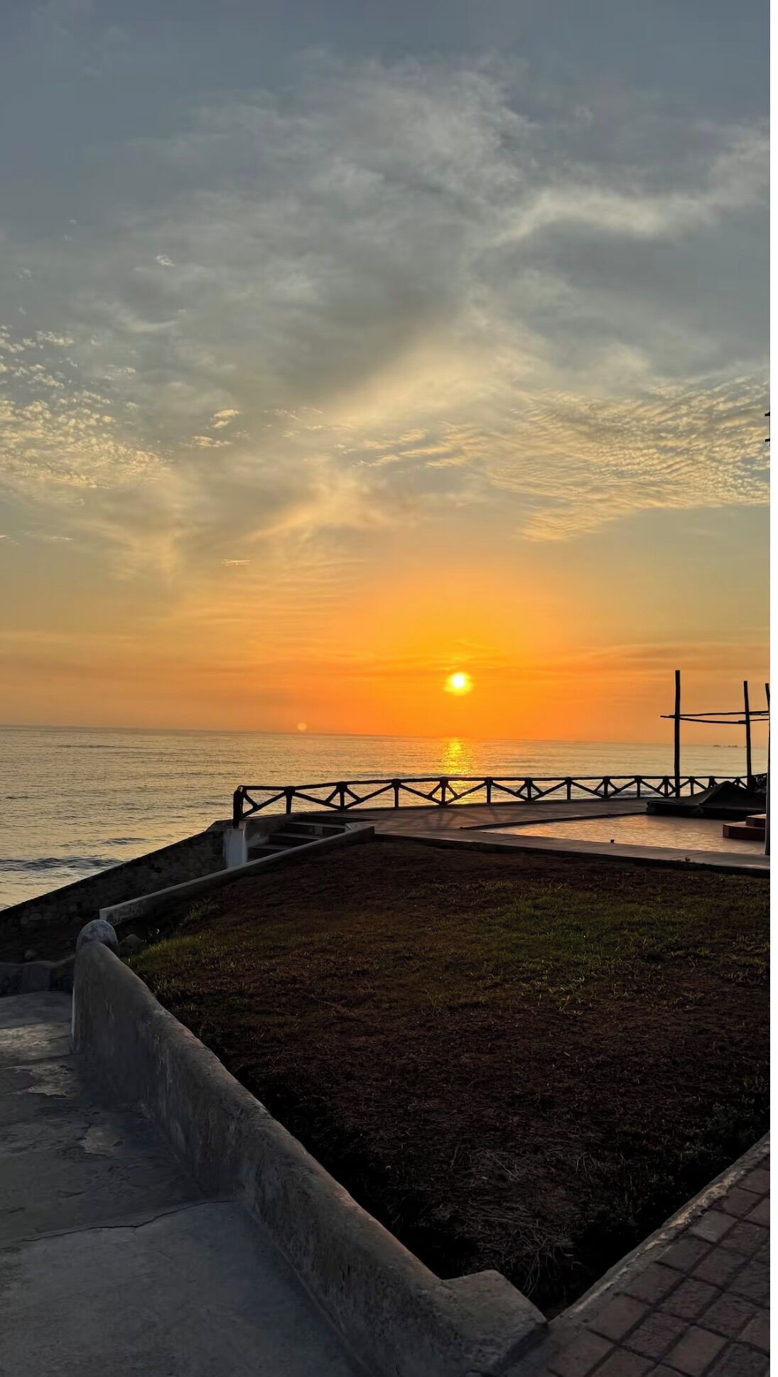 A sunset over the ocean with a concrete viewing platform and a metal railing.