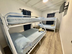 Ein Zimmer mit Etagenbetten, Holzboden, einem an der Wand befestigten Fernseher und einem Fenster mit Vorhängen.