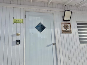 Eine weiße Tür mit Fenster, einem 'Welcome'-Schild und einem 'Zeus'-Schild.