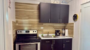 A compact kitchen with a stove, oven, dark cabinets, a coffee maker, and a clock. - Beachside Escape | Patio, Pool, Pet-Friendly & BBQ (Cabo Rojo)