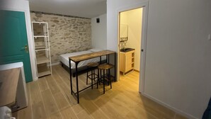 Ett litet rum med en säng, ett litet bord med stolar, en garderob och ett badrum med handfat och spegel.