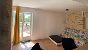 Une pièce comprenant un lit, une petite table, une chaise, une porte avec un rideau et une vue sur l’extérieur.