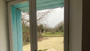 Une porte-fenêtre coulissante donne sur un patio extérieur doté d’un sol carrelé et offrant une vue sur un paysage verdoyant.