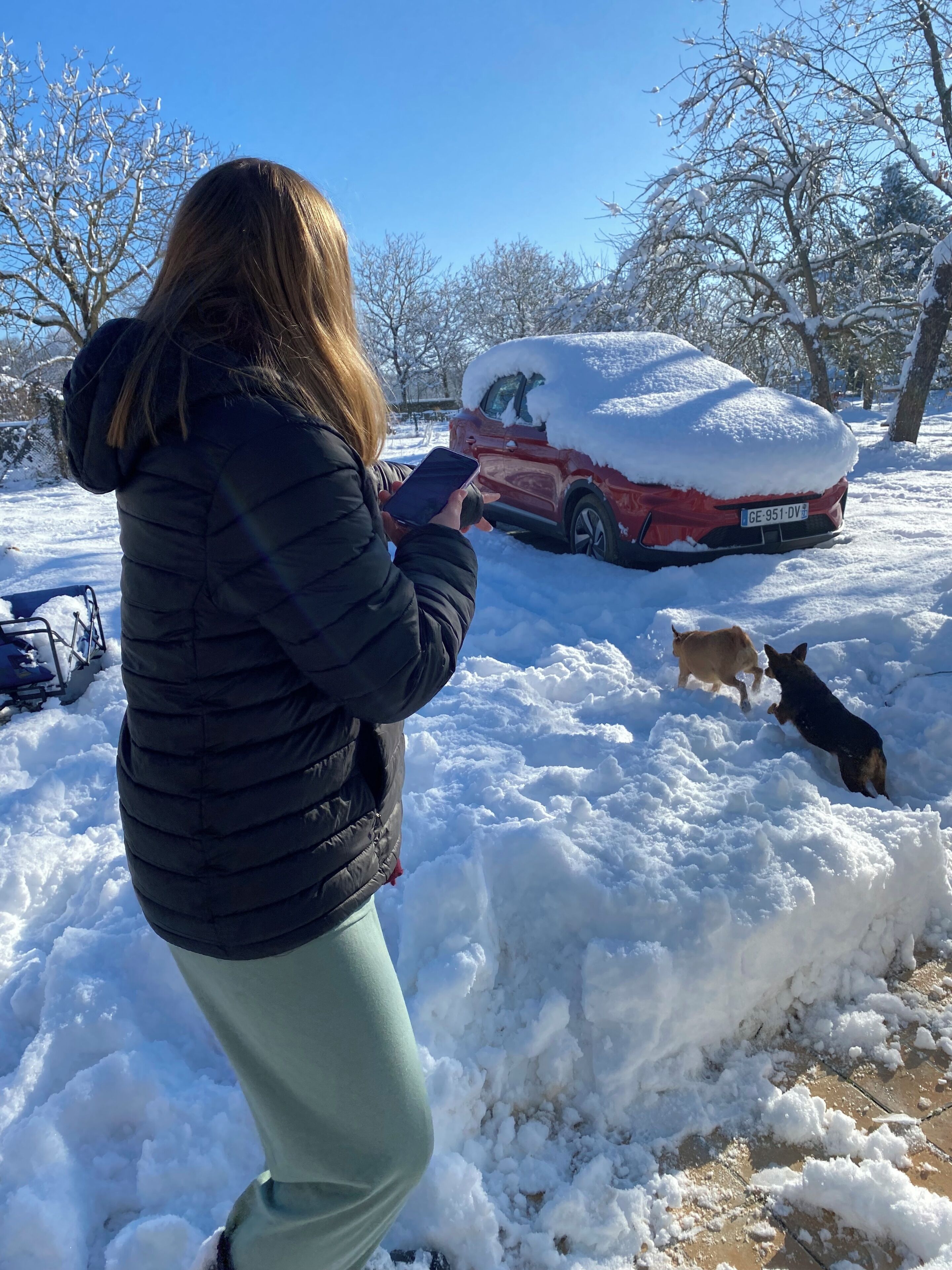 Una persona está de pie en un espacio exterior nevado, con un coche cubierto de nieve al fondo.