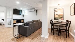 A modern living room with a sofa, a dining table, and chairs. There is a TV mounted on the wall and a plant on the windowsill. - Entire Rental Unit - Cozy 1 BR/ 1 BA (Atlanta)
