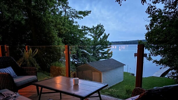 An outdoor deck with wicker furniture, a table, and a view of a lake and distant buildings.