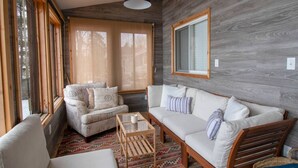 A cozy room with a sofa, armchair, and a small table, wooden walls, and large windows.