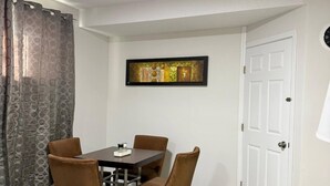 Uma sala de jantar com mesa e cadeiras, um quadro na parede e uma porta branca.